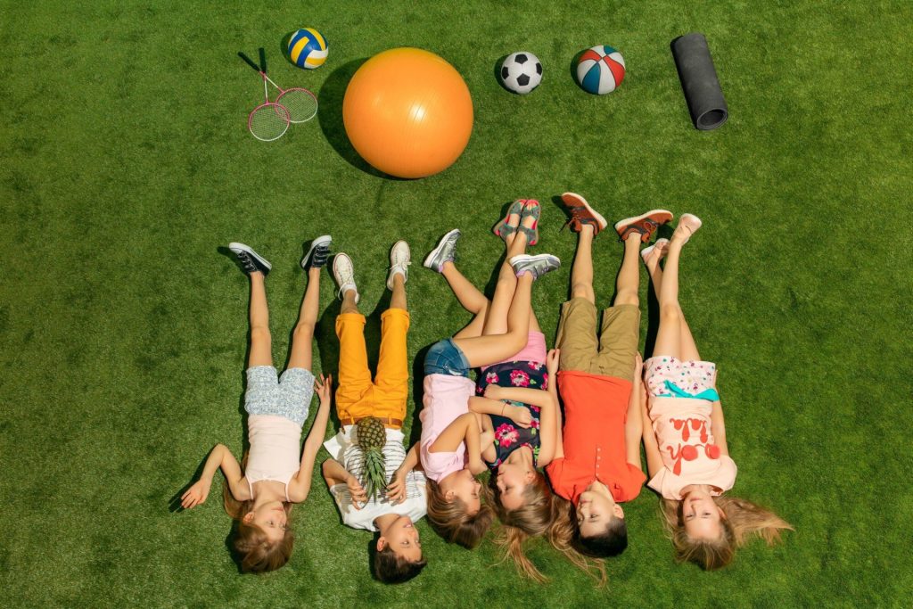 Деца, които лежат на трева след игри в детски лагер LuckyKids ADVENTURE