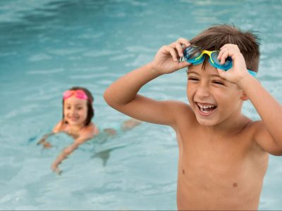 Момче и момиче с плувни очила се забавляват в басейн.